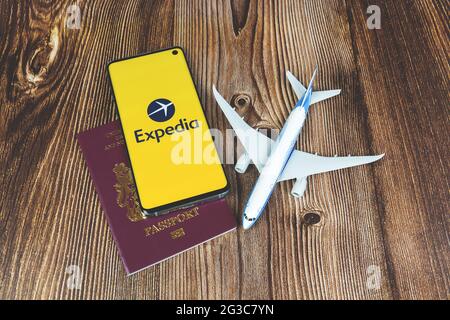 Smartphone mit Expedia App-Logo mit Flugzeugspielzeug und rotem Reisepass auf Holzhintergrund. Reise-Anwendung, Urlaubsplanung Stockfoto