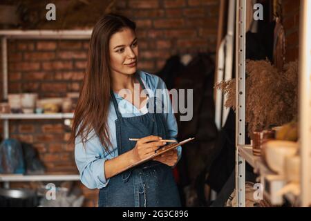 Schöne elegante Handwerk Frau mit langen Haaren hält Zwischenablage in den Händen in der Kunst modernes Studio Stockfoto