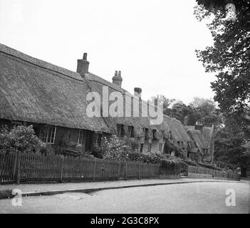 Geschichte aus den 1930er Jahren, auf einem Hügel am Rande des Dartmoor-Nationalparks, eine Reihe von alten reetgedeckten Cottages, Chagford, Devon, England, Großbritannien. Das Strohdach ist ein traditionelles Handwerk und eine Methode, um ein Dach mit trockener Vegetation zu bauen, in der Regel Weizenstroh oder an einigen Stellen Wasserschilf. Die englische Grafschaft Devon, eine sehr alte Dachdeckungsmethode, soll die größte Anzahl historischer reetgedeckter Gebäude der Welt enthalten, in denen Weizenschilf oder einfach „Devon-Schilf“ der Rohstoff war, der von Landwirten, die sich auf die Herstellung von Stroh für reetgedeckte Dächer spezialisiert haben, verwendet wurde. Stockfoto