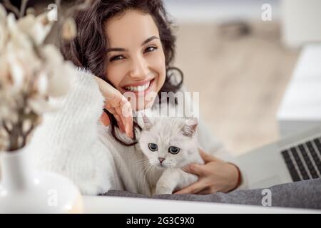 Nette junge Frau, die eine weiße Katze hält und nett lächelt Stockfoto