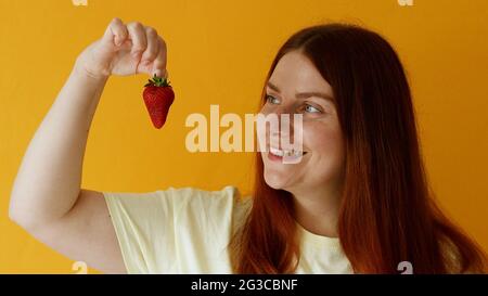 Köstliches Erdbeerdessert. Fröhliche charmante kaukasische Frau lächelt gut gelaunt, wie isst Lieblings-Dessert hält rote Beere. Stockfoto