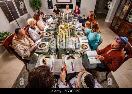 Am traditionellen Esstisch für ein Passahseder in einem jüdischen Haus in Südkalifornien lasen die Gäste die Haggadah, einen jüdischen Text, der die darlegt Stockfoto