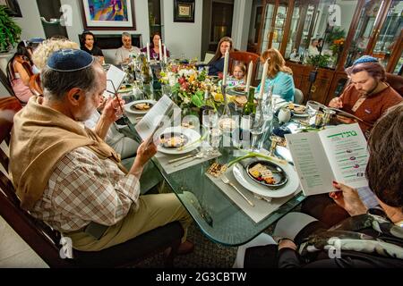 Am traditionellen Esstisch für ein Passahseder in einem jüdischen Haus in Südkalifornien lasen die Gäste die Haggadah, einen jüdischen Text, der die darlegt Stockfoto