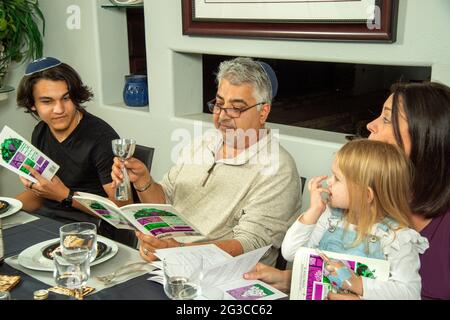 Am traditionellen Esstisch für ein Passahseder in einem jüdischen Haus in Südkalifornien lasen ein Ehemann, eine Ehefrau, ein Sohn und eine Enkelin die Haggadah, A Stockfoto