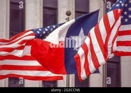 DIE US- und Texas-Staatsflaggen stehen nebeneinander, während sie im Wind auf Fahnenmasten vor einem Bürogebäude in Houston wehen. Stockfoto