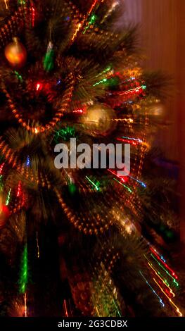 Lichter am Weihnachtsbaum im Fokus mit zwei Sekunden Belichtung beim Zoomen, um abstrakte Lichtstreifen zu erzeugen. Stockfoto