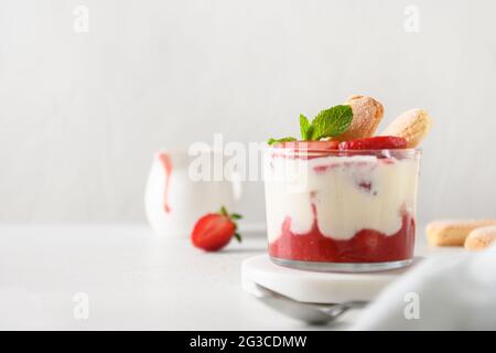 Sommerdessert in mehreren Lagen in Gläsern mit Plätzchen Savoyardi, Mascarpone und mit Schlagsahne verzierten Erdbeeren. Nahaufnahme. Italienische Tiramisu mit Summe Stockfoto