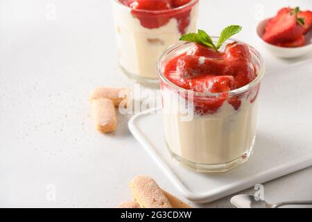Sommerdessert in mehreren Lagen in Gläsern mit Plätzchen Savoyardi, Mascarpone und mit Schlagsahne verzierten Erdbeeren. Nahaufnahme. Italienische Tiramisu mit Summe Stockfoto