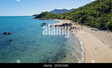 Ein abgeschiedener Sandstrand, übersät mit Felsen bei Ebbe und kristallklarem Wasser, das bis zum Meeresboden hindurchgeht Stockfoto