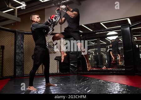Professionelle mma Kämpfer lehrt Selbstverteidigung Tricks, zeigt es jungen Boxer. Üben Sie verschiedene Techniken zusammen. Sport, Workout-Konzept. Seite Stockfoto