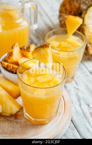 Leckerer Ananassaft in zwei Gläsern mit Ananasscheiben. Frischer natürlicher Ananascocktail und Saft im Glaskrug auf weißem Holztisch Stockfoto