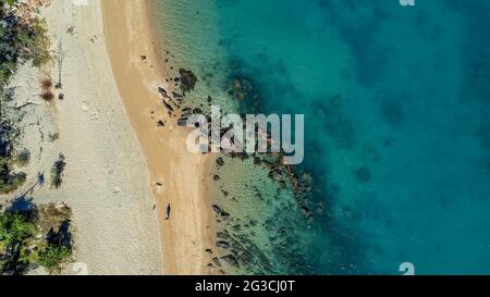 Ein Mann und sein Hund laufen am Strand weit unter einer Drohne, die bei Ebbe über einem tropischen Strand fliegt, mit Felsen, die aus dem Wasser und der Detai zeigen Stockfoto