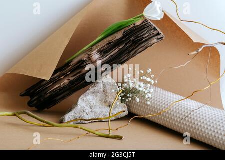 Kreative abstrakte minimalistische monochrome Boho Stillleben Komposition mit natürlichen Materialien Stein Holz Papier Blume Pflanze trockene Zweige auf braunem Handwerk Stockfoto