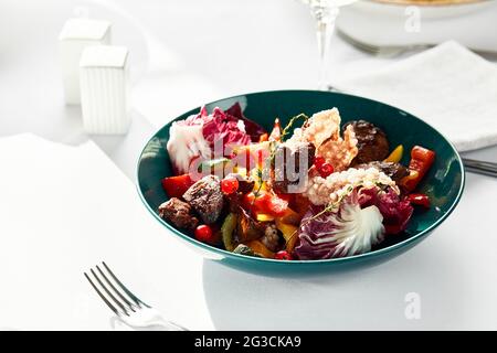 Kalbsleber mit Salat und Mango- und Orangenscheiben, Nahaufnahme, heller Hintergrund, weiße Gerichte. Stockfoto