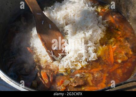 Kochen traditioneller orientalischer Pilaf in einem Kessel über einem Feuer. Der gewaschene Reis wird in einen Zervak für das Eintopf Fleisch und Gemüse gegossen. Stockfoto