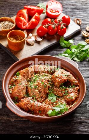 Chakhokhbili, geschmortes Huhn, Tomate mit frischen Kräutern, Walnüssen und Gewürzen in einem Tontopf auf einem Holztisch, georgische Küche, vertikale Ansicht Stockfoto