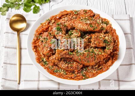 Chakhokhbili, geschmortes Huhn, Tomate mit frischen Kräutern, Walnüssen und Gewürzen auf einem weißen Teller auf einem Holztisch, georgische Küche Stockfoto