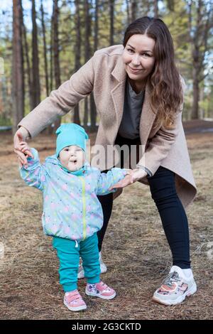 Mutter lehrt Baby, im Park zu gehen, erster Schritt der entzückenden kaukasischen kleinen Mädchen mit Mutter Hilfe Stockfoto