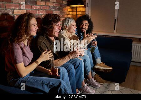 Diverse Studenten, die gerne in Videospielen spielen, ruhen sich zu Hause aus. Lächelnd überrascht aufgeregt amerikanischen Menschen haben Spaß mit Joysticks im Wohnzimmer int Stockfoto
