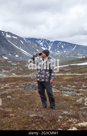 Junger Mann, der auf dem Handy spricht, mit jemandem während des Naturspaziergangs, in den Bergen in der Frühjahrssaison spricht Stockfoto