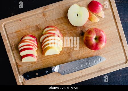 Honeycrisp-Äpfel in Scheiben auf einem Bambus-Schneidebrett: Scheiben roter Äpfel auf einem hölzernen Schneidebrett Stockfoto