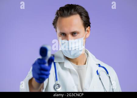 Der Arzt in weißem medizinischen Mantel leitet ein elektronisches berührungsloses Thermometer in die Kameralinse und misst die Temperatur. Stockfoto