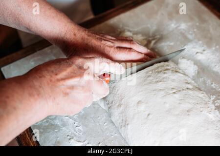 Weibliche Hände schneiden Stücke von rohem hausgemachtem Brotgebäck auf dem Tisch. Hausgemachte Küche Stockfoto