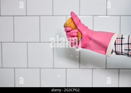 Hand in Gummihandschuh hält Schwamm zum Spülen, isoliert auf weiß geflieste Wand. Reinigung, Waschkonzept Stockfoto