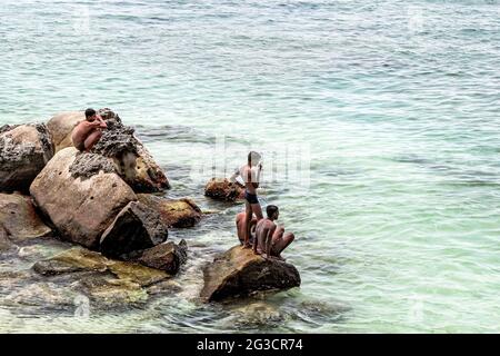 Menschen vor Ort, die auf Felsen an der Küste von Mirissa in Sri Lanka sitzen Stockfoto