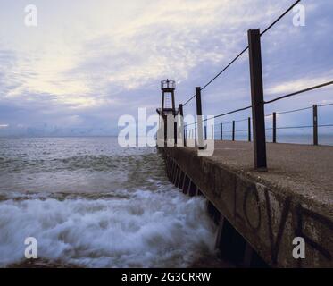 Leuchtturm am Ende eines Steinpiers unter dem wolkigen Himmel Stockfoto