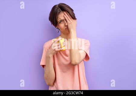 Weinende Frau braucht mehr Ruhe, Weibchen ist müde von der Arbeit, will nicht zur Arbeit gehen oder studieren, hält Becher oder Tasse in den Händen. Isolierter violetter Hintergrund Stockfoto