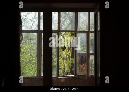 Holzfenster auf dem alten Balkon. Blick vom Fenster auf die Straße. Fensterrahmen in der Wohnung. Morgenlicht draußen. Stockfoto