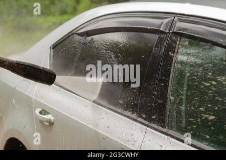 Autowäsche. Das Auto wird unter dem Druck eines Wasserstrahls gewaschen. Mit einem Wasserspray Schmutz von der Fahrzeugoberfläche abwaschen. Stockfoto