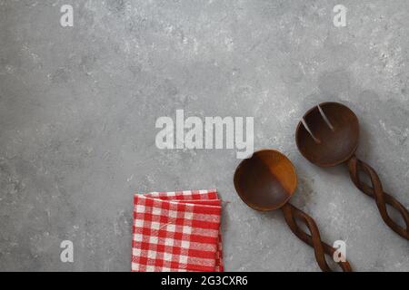 Holzlöffel und karierte Tischdecke auf steinernem Hintergrund Stockfoto