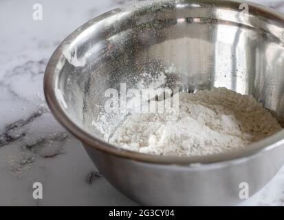 Runde Metallschüssel, gefüllt mit weißen Zutaten auf einer Marmoroberfläche mit natürlichem Licht Stockfoto