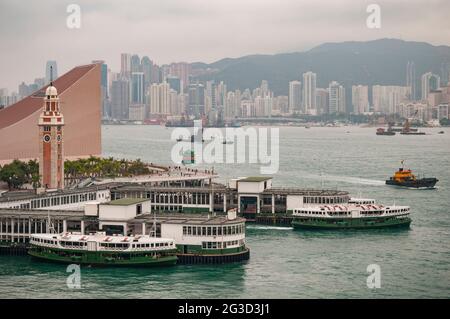 Zwei ikonische Star Ferries am Fähranleger in Tsim Sha Tsui, Kowloon, mit Victoria Harbour und Causeway Bay auf Hong Kong Island im Hintergrund Stockfoto