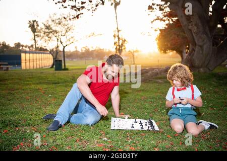 Vater und Sohn spielen Schach auf Gras im Sommerpark, Kindheit Stockfoto
