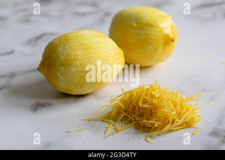 Zwei volle Zitrone mit der Schale, die von einem Zester geriebenen und einem Stapel von Zest auf einer Marmoroberfläche mit natürlichem Licht Stockfoto