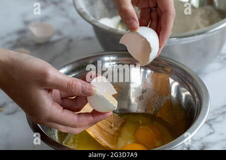 Die Hand einer Frau mit einem aufgerissenen Ei über einer gewickelten Metallmischschüssel mit natürlichem Licht Stockfoto