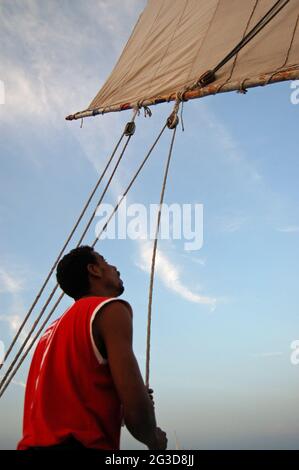 Luxor, Ägypten - 6. Januar 2006: Ein ägyptischer Segler, der die Seile betreibt, die das Segel auf einem traditionellen Felucca-Boot im Abendlicht in L positionieren Stockfoto