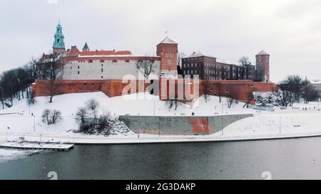 Drohnenansicht des Königsschlosses Wawel. Im Vordergrund das Ufer der Weichsel. Panoramablick auf die Skyline der Stadt während der Wintersaison. Der klare weiße Himmel im Hintergrund. Schneebedeckte Straßen. Stockfoto