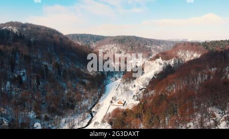Schneebedeckte Straße zwischen immergrünen Bäumen im Ojcowski Park Narodowy Krakau, Polen. Schlampige Gegend mit üppigem Grün. Panoramablick. Schöner, wolkig blauer Himmel im Hintergrund. Stockfoto