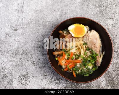 Ramen mit Pilzen und Huhn in einer Schüssel auf dunklem Grund. Draufsicht, flach liegend Stockfoto