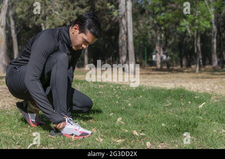 Der hispanische Mann trägt Sportkleidung und schnürte seine Turnschuhe im Park Stockfoto