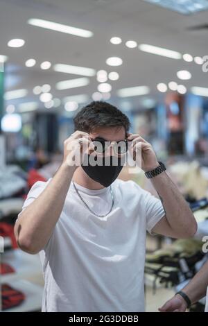 Vertikale Aufnahme eines stylischen jungen Spanierers, der im Einkaufszentrum eine Sonnenbrille anprobiert Stockfoto