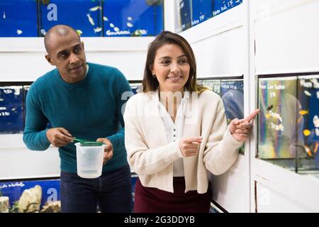 Positiver Verkäufer hilft Frau bei der Auswahl von Aquarienfischen Stockfoto