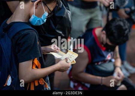 Hongkong, China. Juni 2021. Ein Junge hält einen Aufkleber mit der Aufschrift Go auf Chinesisch.Dutzende von Menschen legten weiße Blumen, Bänder und zündeten Kerzen an, um an den zweijährigen Tod von Marco Leung Ling-Kit in Admiralty, Hongkong, zu erinnern. Er war ein Mann, der während einer sozialen Unruhen in einem gelben Regenmantel vom Gerüst eines nahegelegenen Gebäudes zu Tode fiel und zu einer Ikone für die Proteste in Hongkong im Jahr 2019-2020 geworden war. Kredit: SOPA Images Limited/Alamy Live Nachrichten Stockfoto