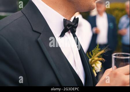 In der Mitte des Bräutigams in einem formellen Anzug mit einem Glas Getränk Stockfoto