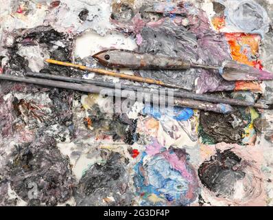 Eine vollständige Ansicht einer Künstlerpalette, die mit satter, dichter, nasser Ölfarbe, Pinsel und Modelliermesser beladen ist. Isoliert auf weißem Hintergrund Stockfoto
