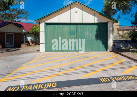 Gelbe diagonal gestrichene Linien auf einer betonierten Auffahrt markieren eine Parkplatzzone vor einer alten Fibro-Doppelgarage in Sydney, Australien Stockfoto